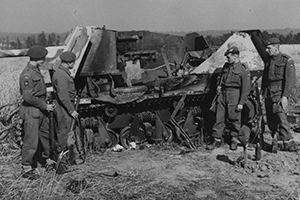 Four paratroopers stand with a burned out Hotchkiss tank chassis.