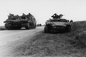 A Priest self-propelled gun passes a Humber Scout car