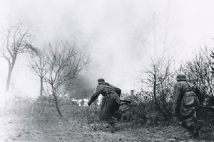 Two German soldiers advance towards burning vehicles